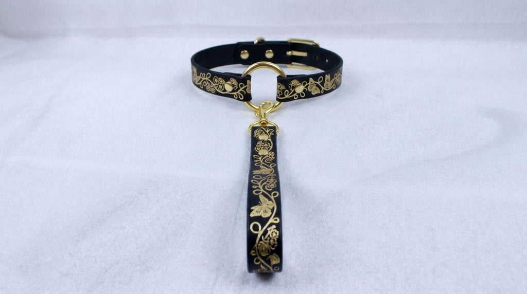 A black collar with gold floral designs and a gold-colored leash attached to it.