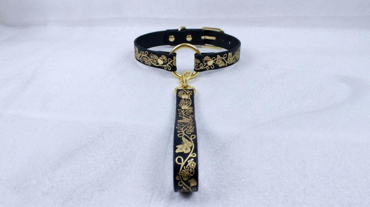 A black collar with gold floral designs and a gold-colored leash attached to it.
