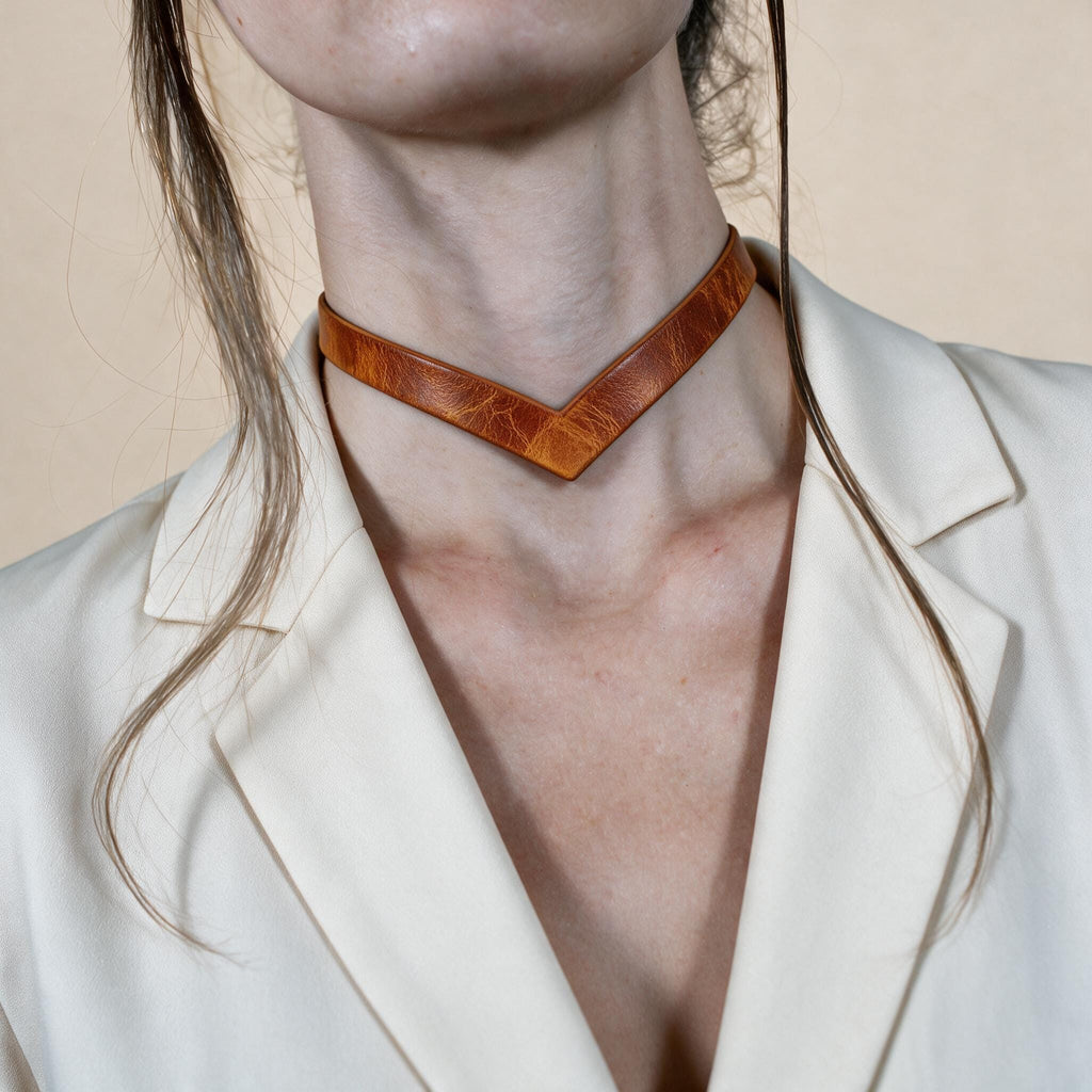 A close-up of a person wearing a white blazer and a leather choker necklace.