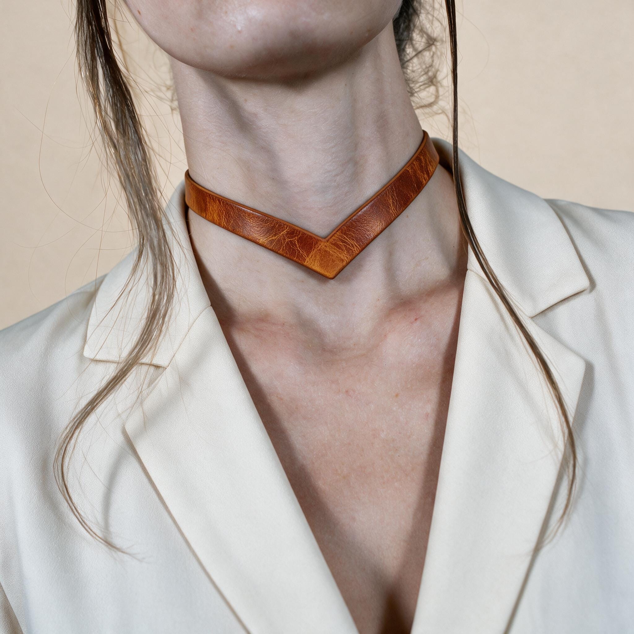 A close-up of a person wearing a white blazer and a leather choker necklace.