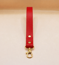 A red leather strap with a gold metal clasp and hook is shown against a light background.