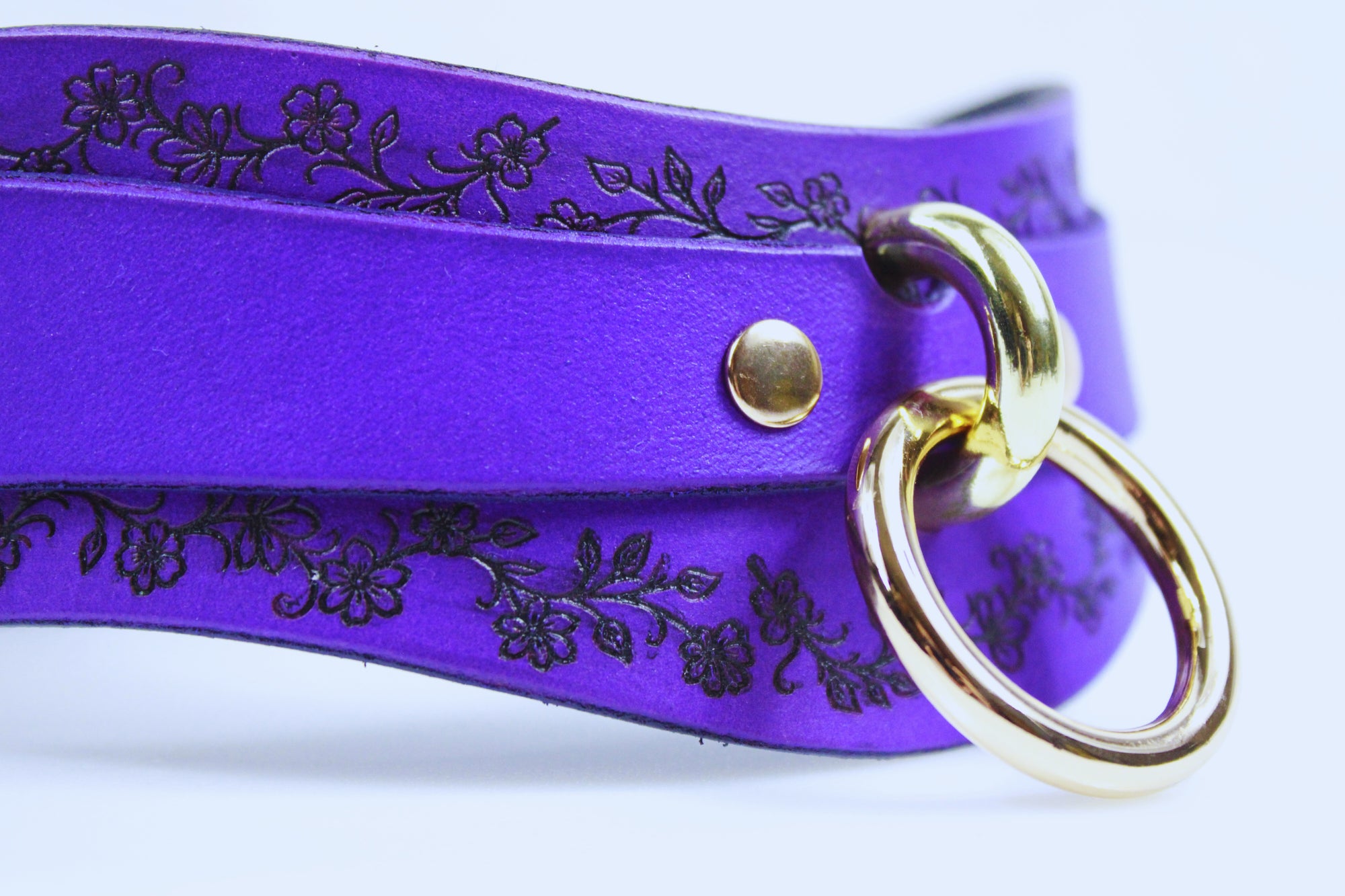 A close-up view of a purple leather choker necklace with a gold-colored ring and a floral design on the clasp.