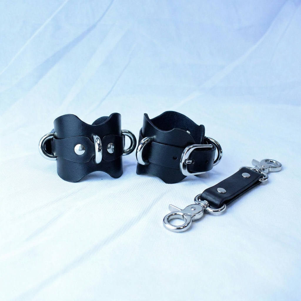 a pair of black leather straps with metal buckles and a metal attachment, placed on a white background.