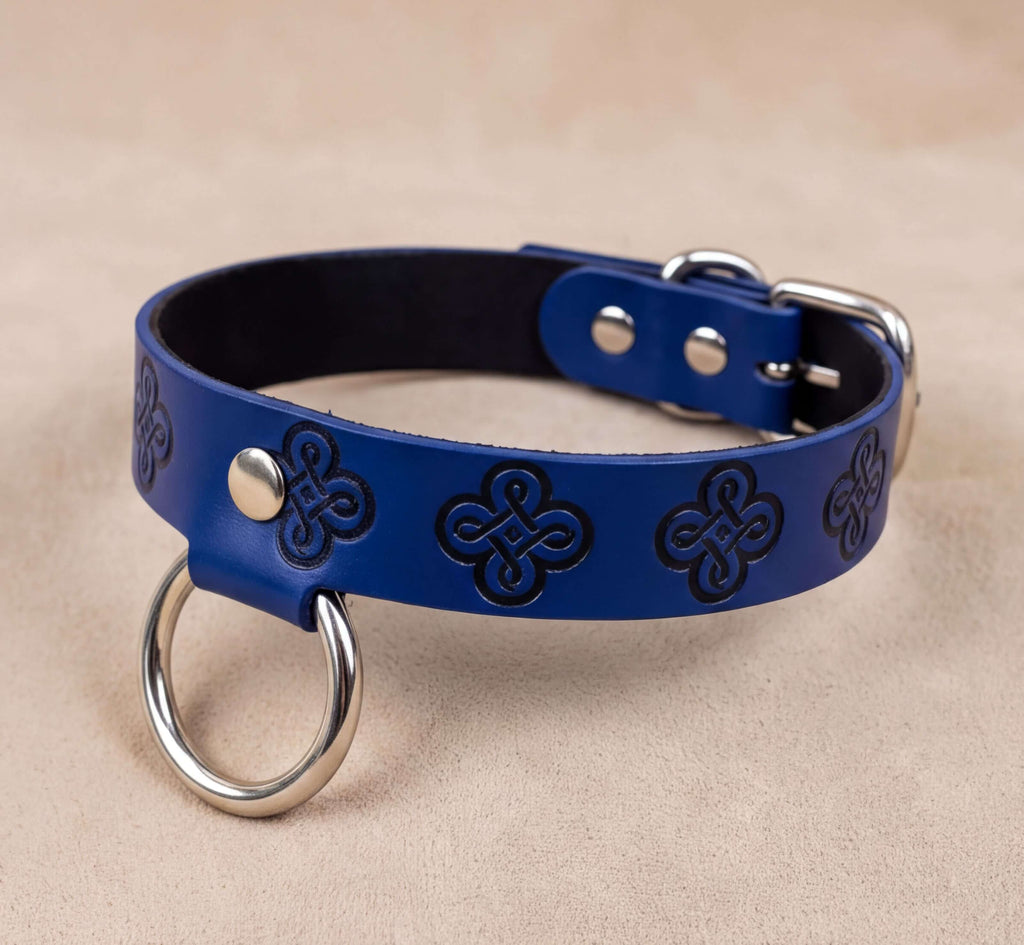 A blue leather dog collar with metal rings and a buckle, placed on a beige surface.
