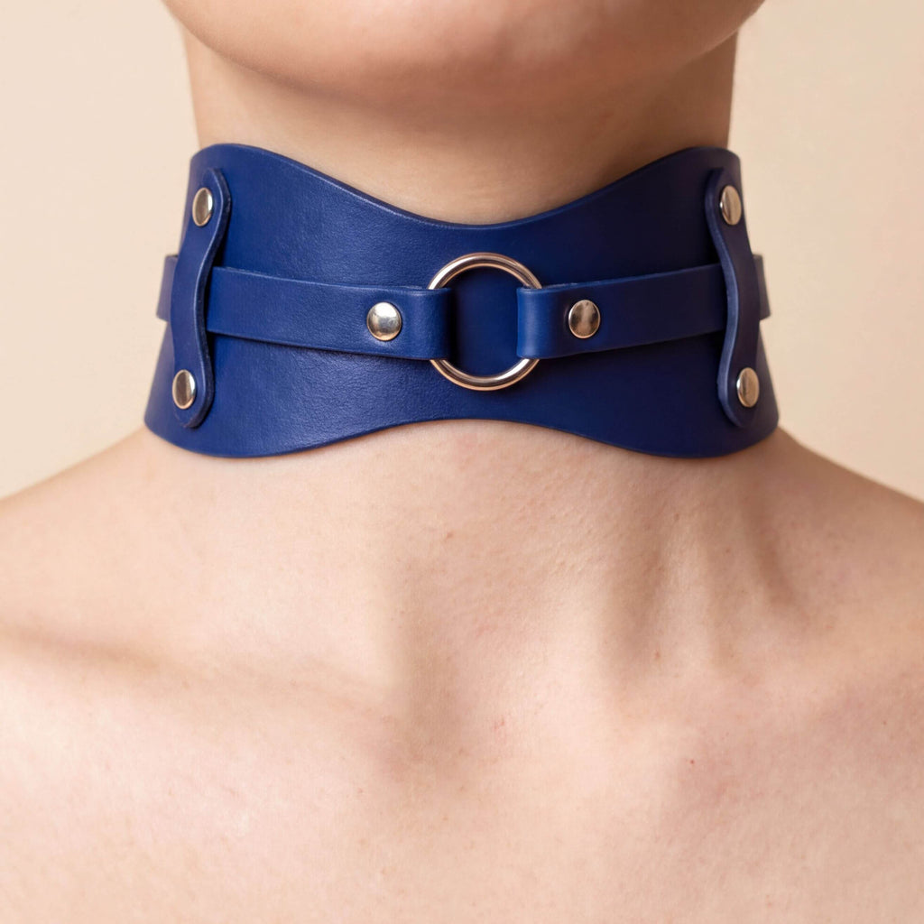 A close-up image of a person wearing a blue leather choker necklace with metal rings and buckles.
