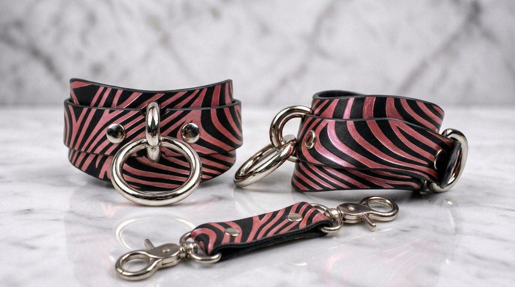 a pair of zebra-striped leather straps with metal rings and buckles, displayed on a marble surface.