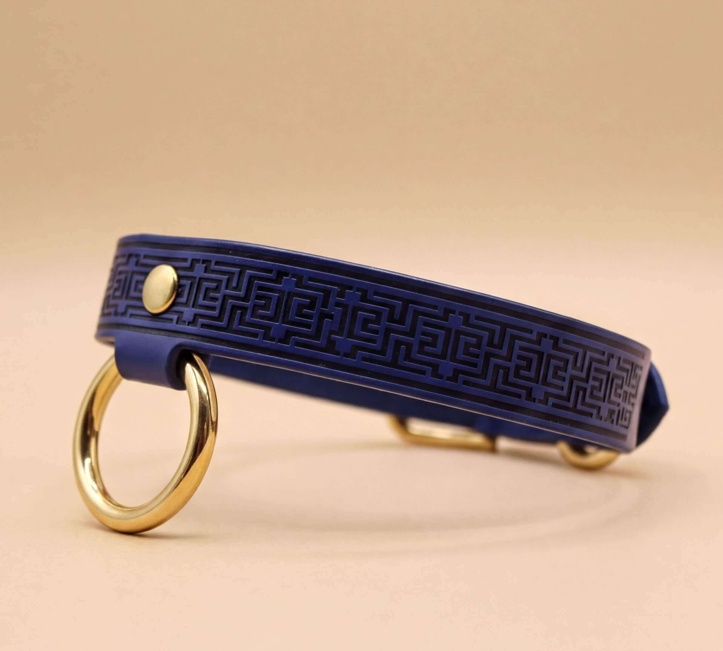 A blue leather collar with a gold-colored metal ring and a geometric pattern design.