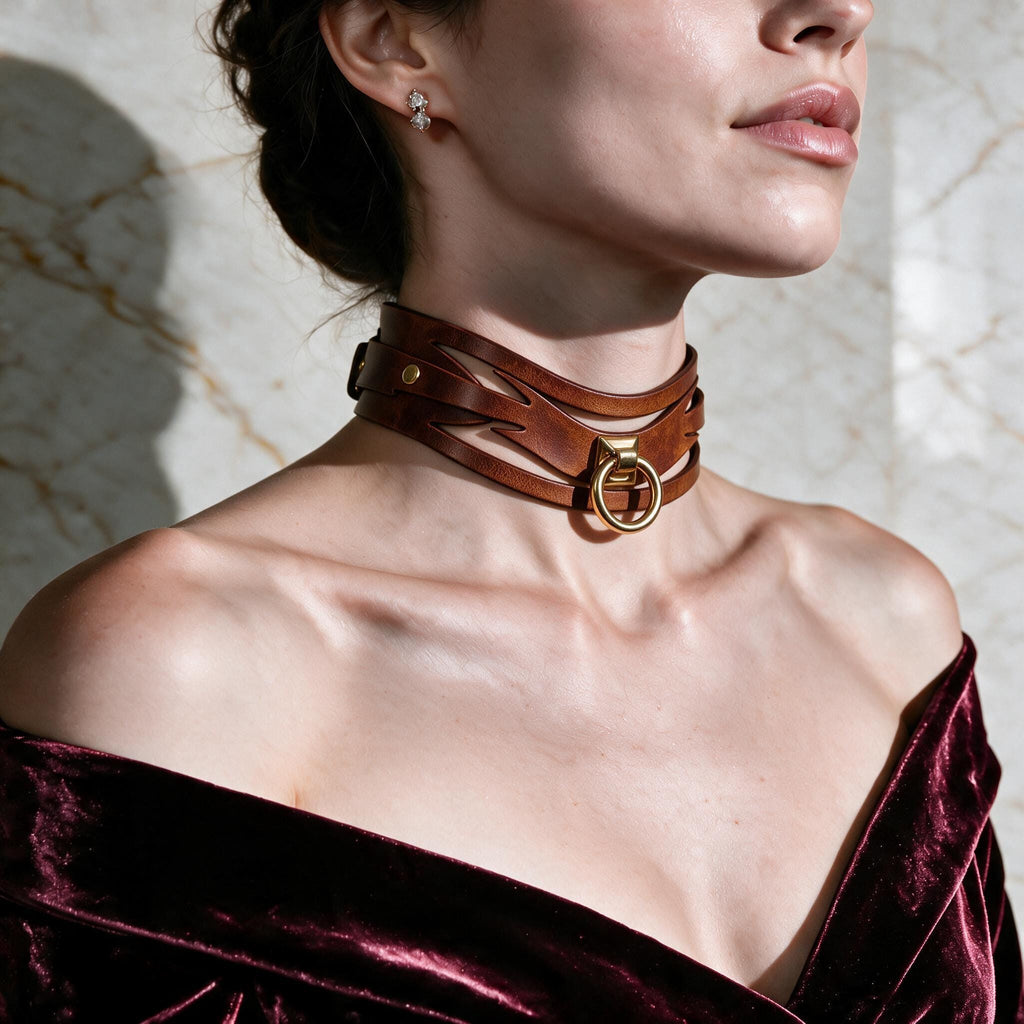 A woman wearing a brown leather choker necklace with a gold buckle, posing against a marble wall.