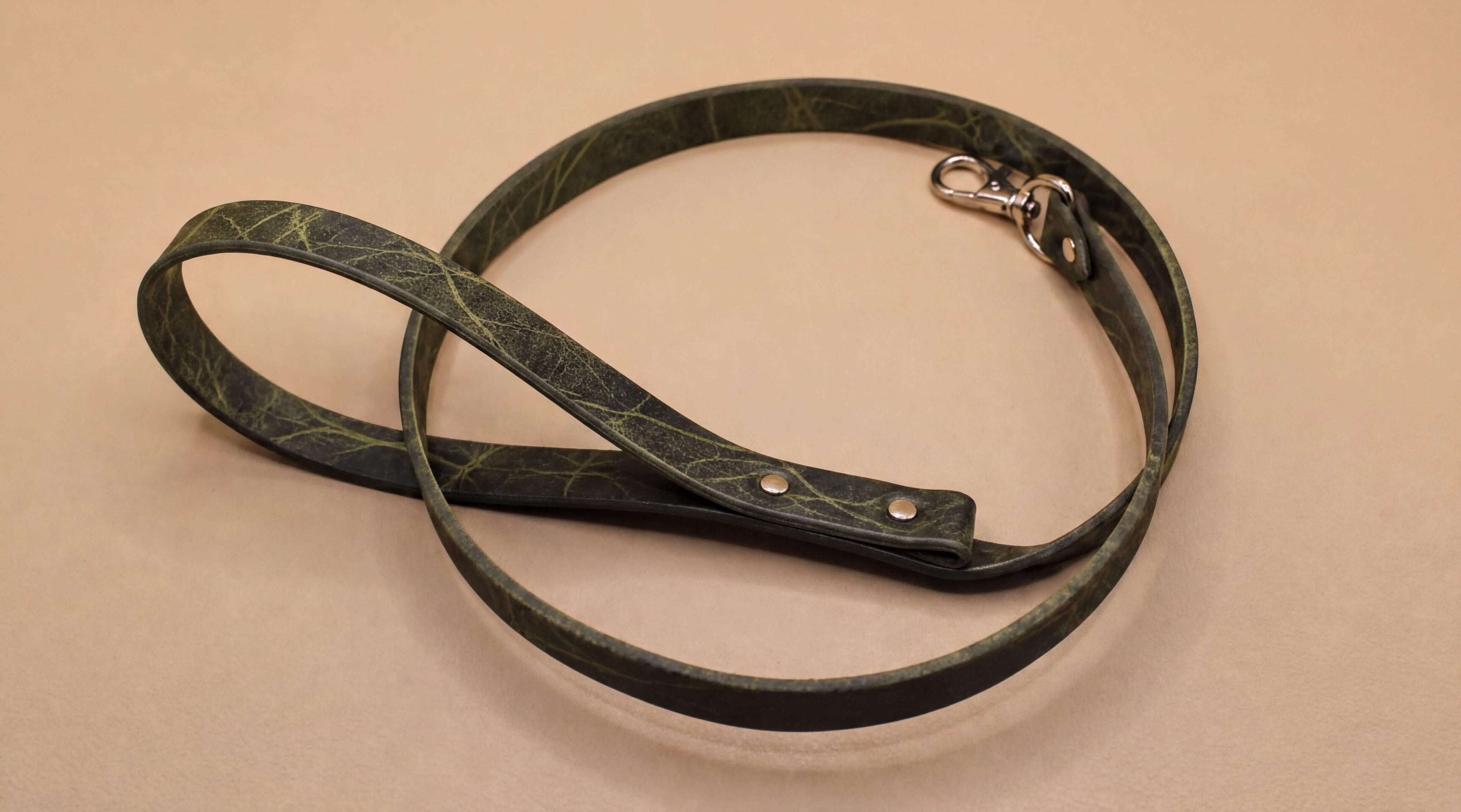 A green leash with a metal clasp and buckle is shown on a beige surface.