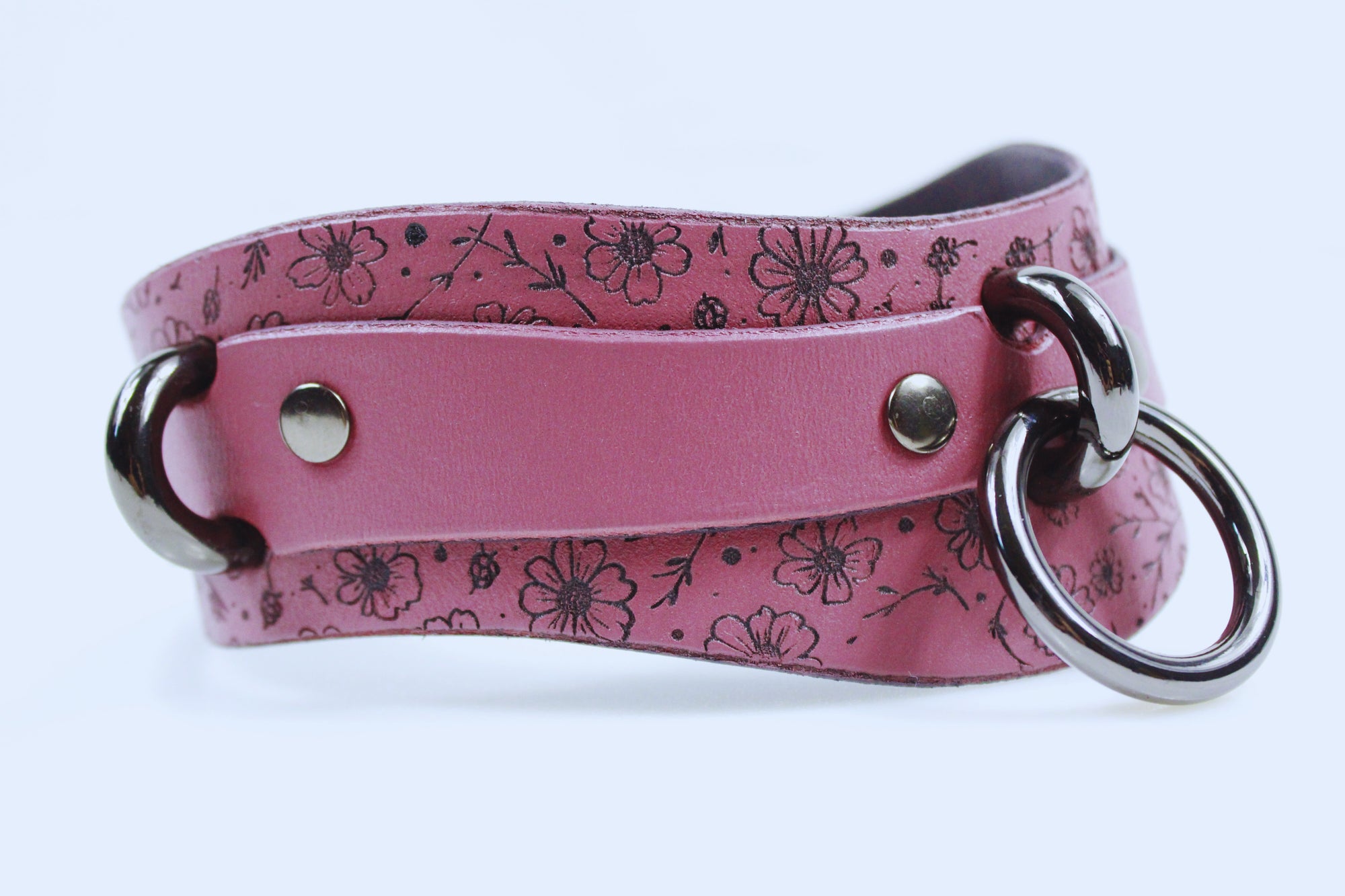 A pink leather choker necklace with a floral pattern and metal rings.