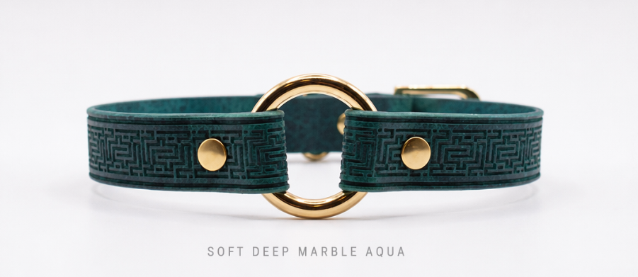A close-up image of a green leather collar with a gold-colored metal ring and two gold-colored metal buttons.