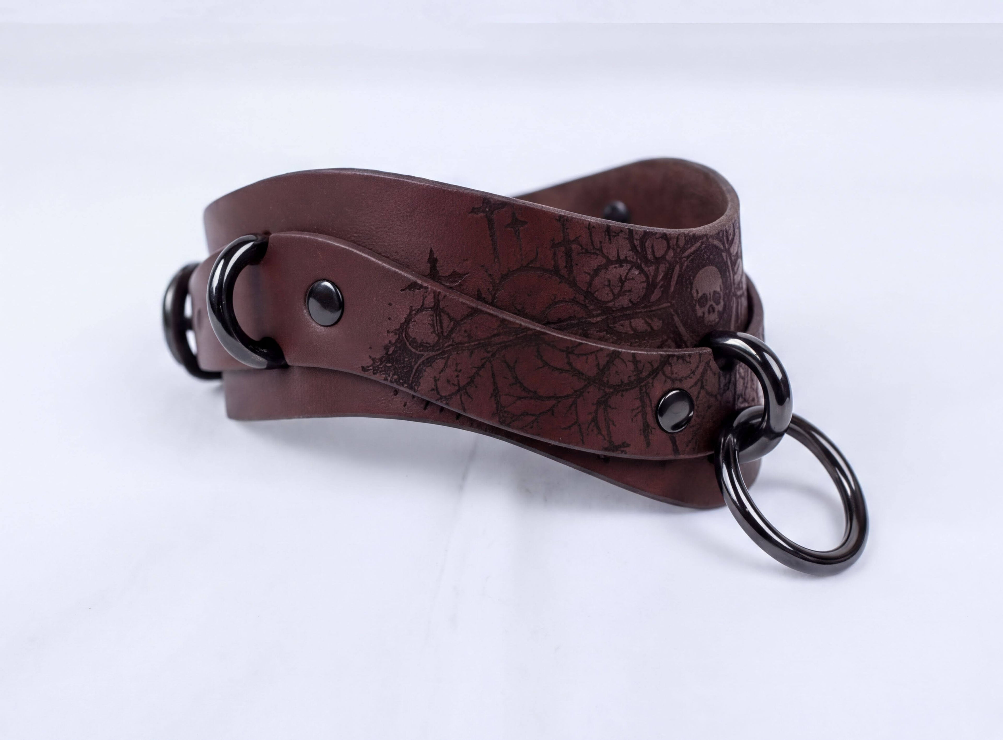 A brown leather strap with metal rings and a floral pattern on it.
