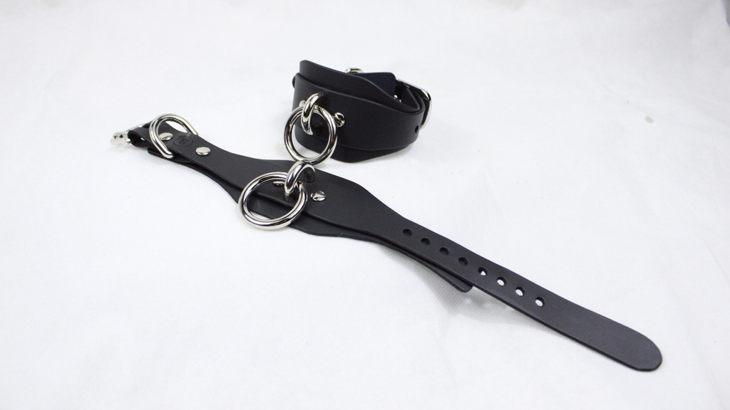 A black leather strap with metal rings and holes is shown on a white background.