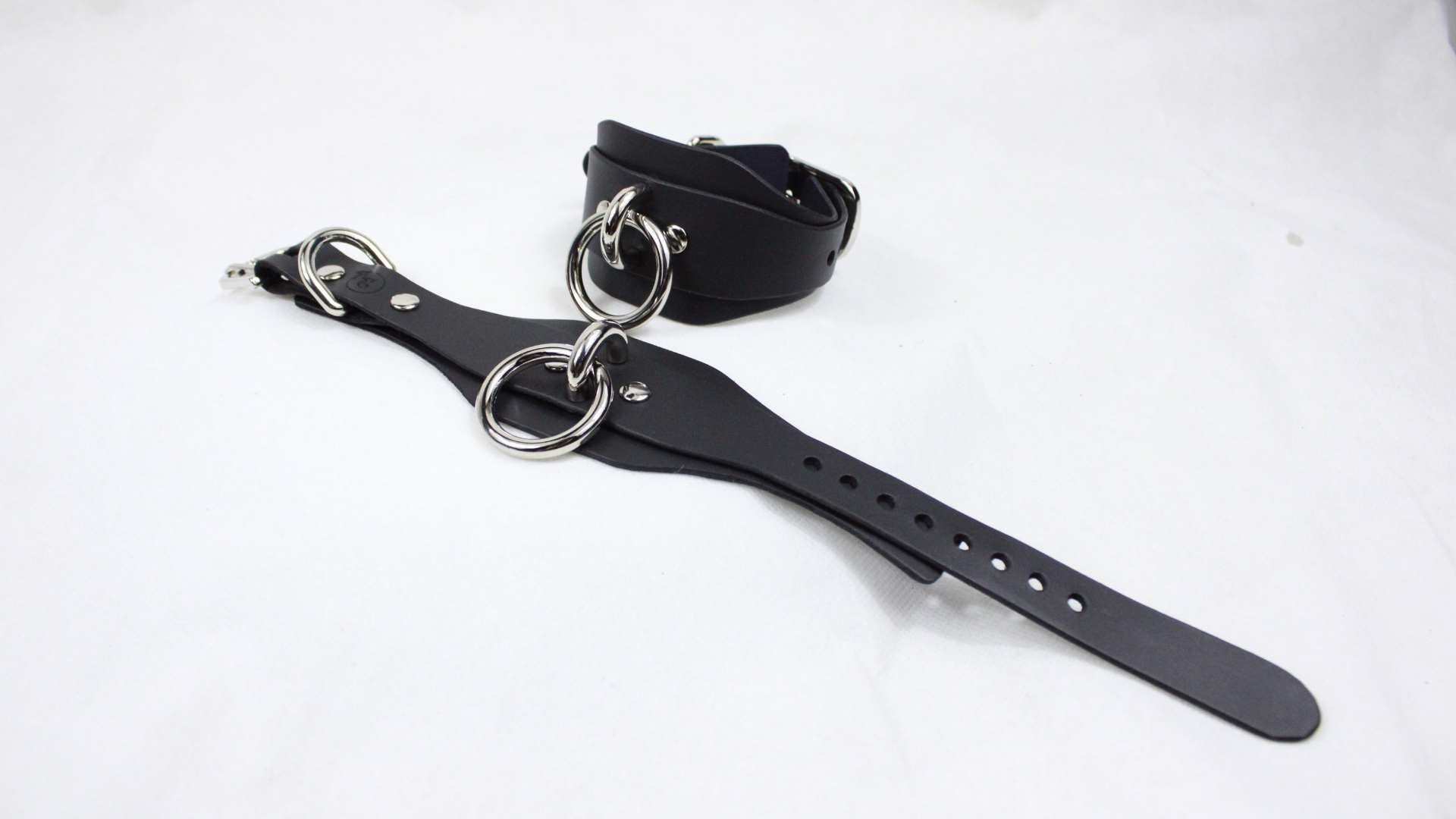 A black leather strap with metal rings and holes is shown on a white background.