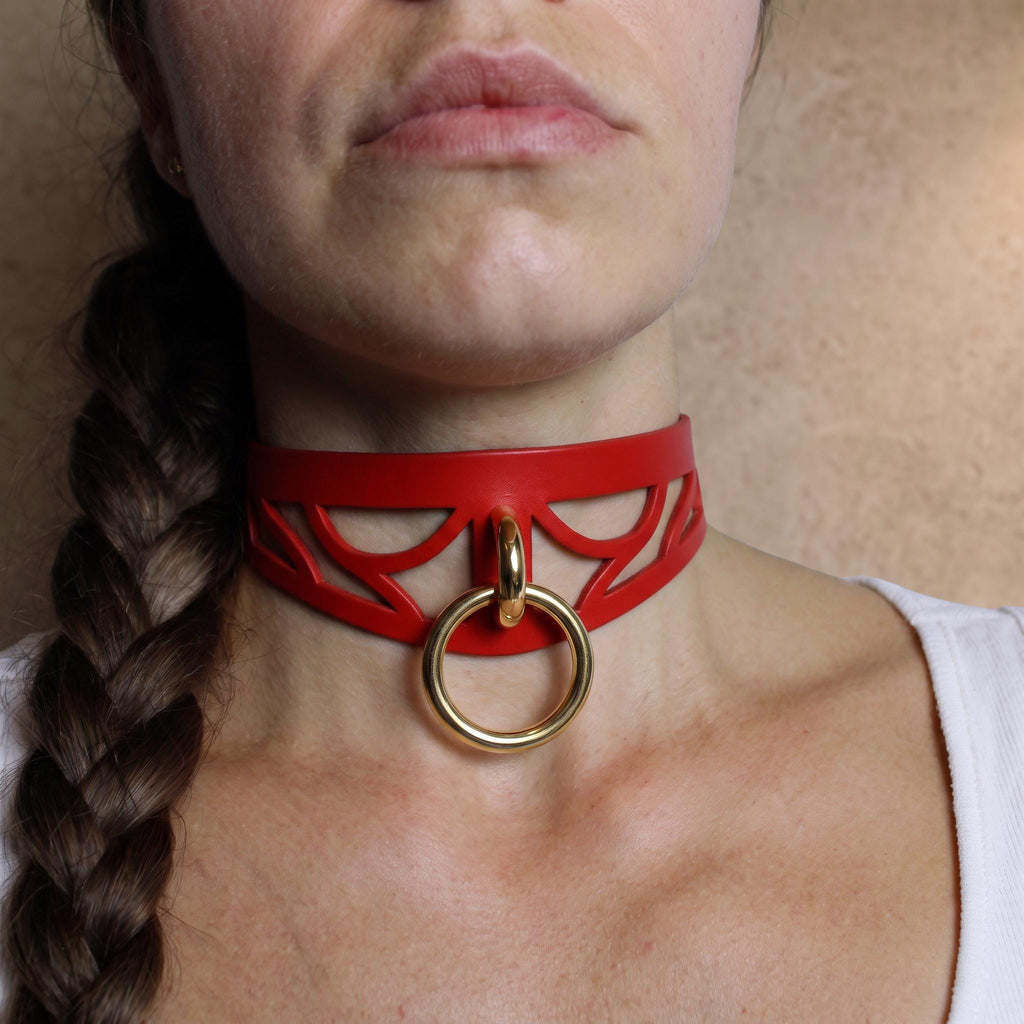 A close-up of a woman's neck and chest area, featuring a red choker necklace with a gold ring.