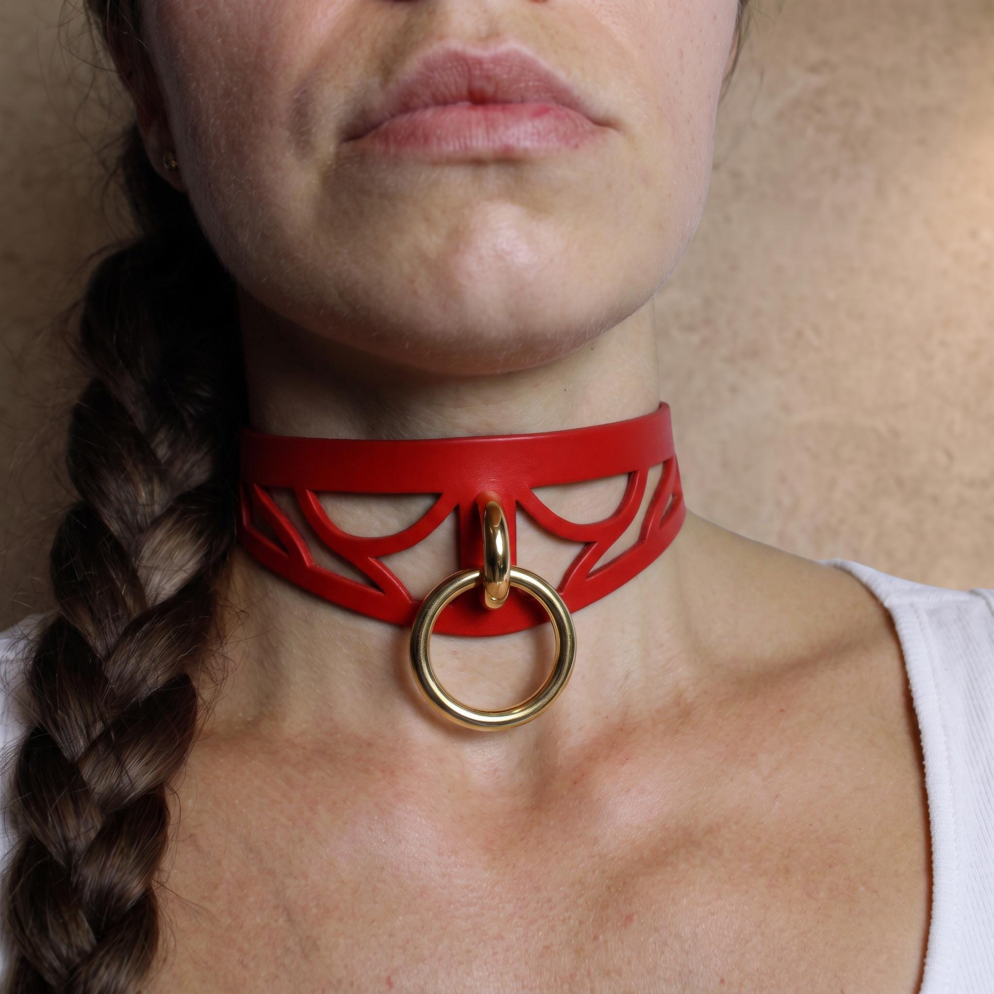 A close-up of a woman's neck and chest area, featuring a red choker necklace with a gold ring.