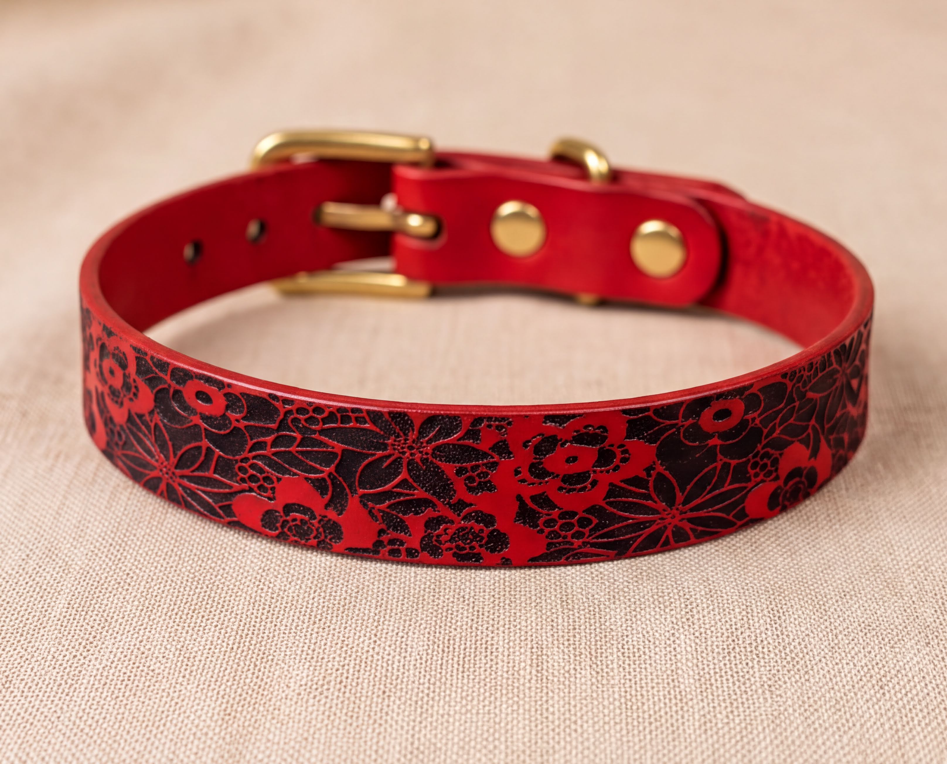 A red leather dog collar with a floral pattern on it.
