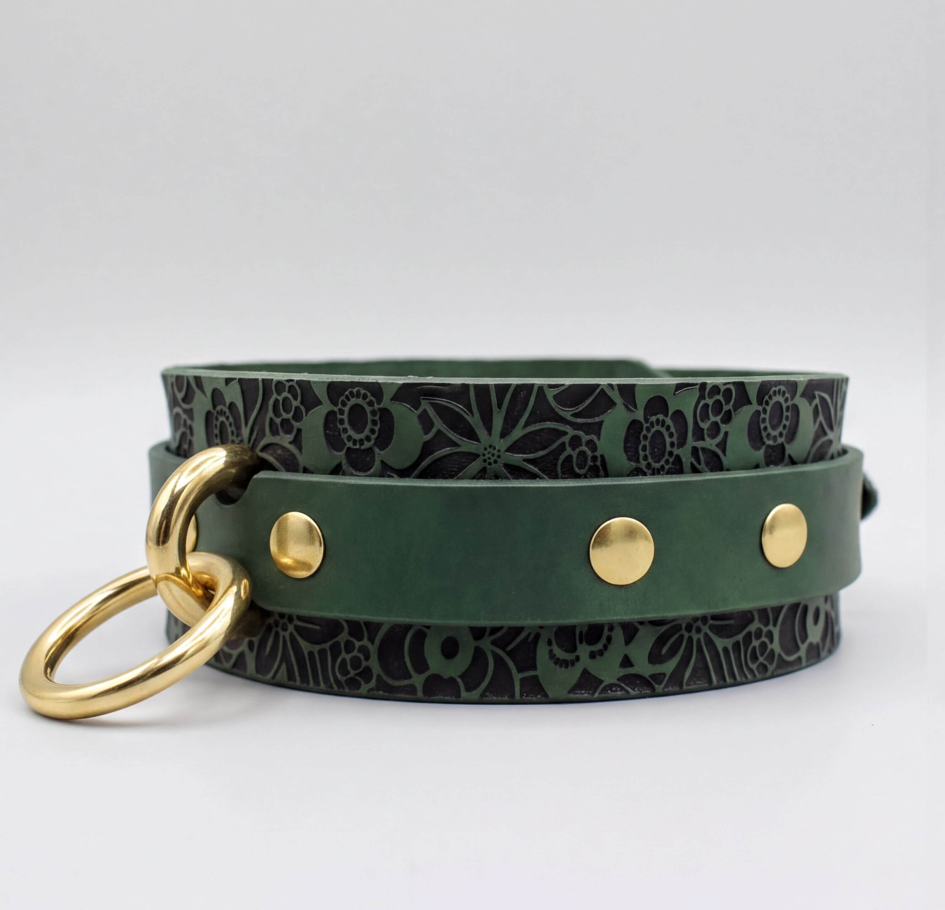 A green leather collar with a floral pattern and gold metal rings.