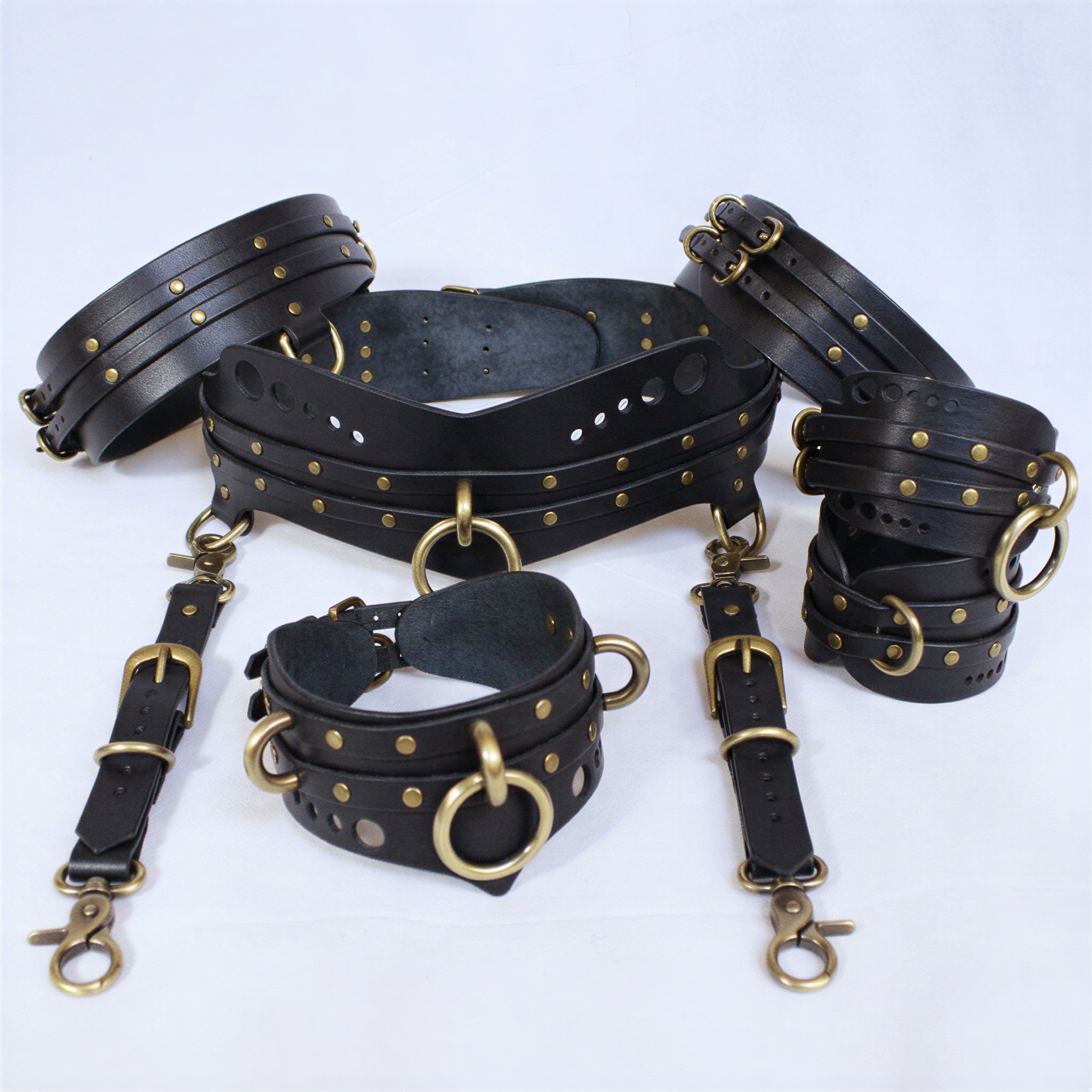 A collection of black leather straps with gold-colored buckles and studs, arranged on a white background.
