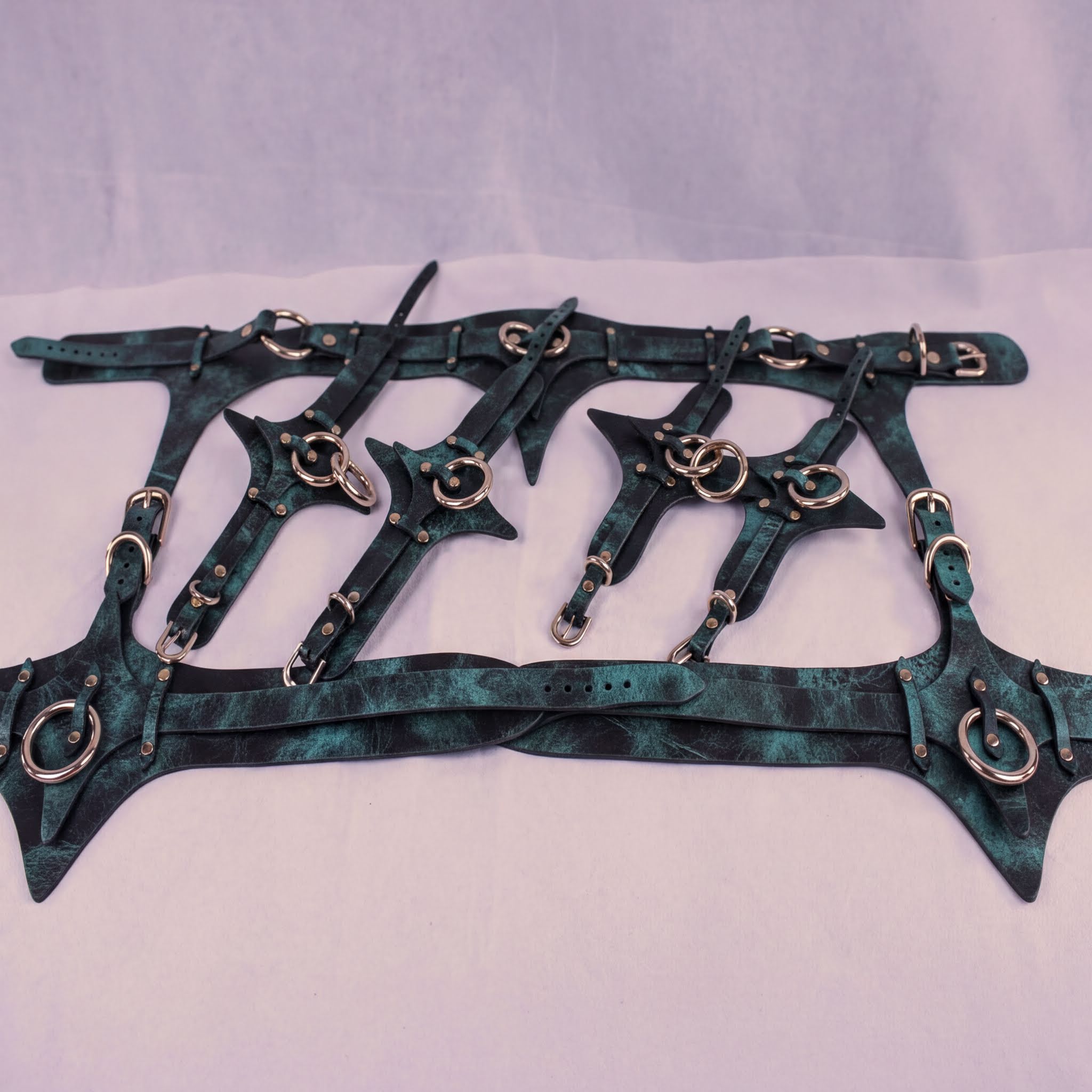 A collection of dark green leather straps with metal studs and buckles, arranged in a grid-like pattern.