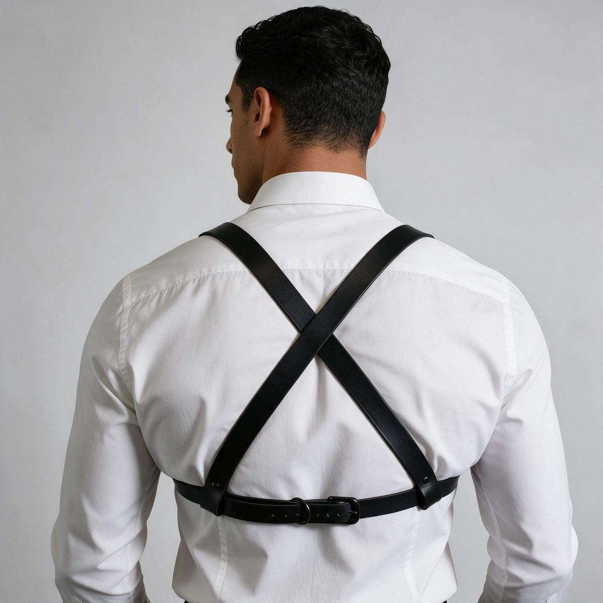 A man wearing a white dress shirt and a black leather harness with a black strap across his back.