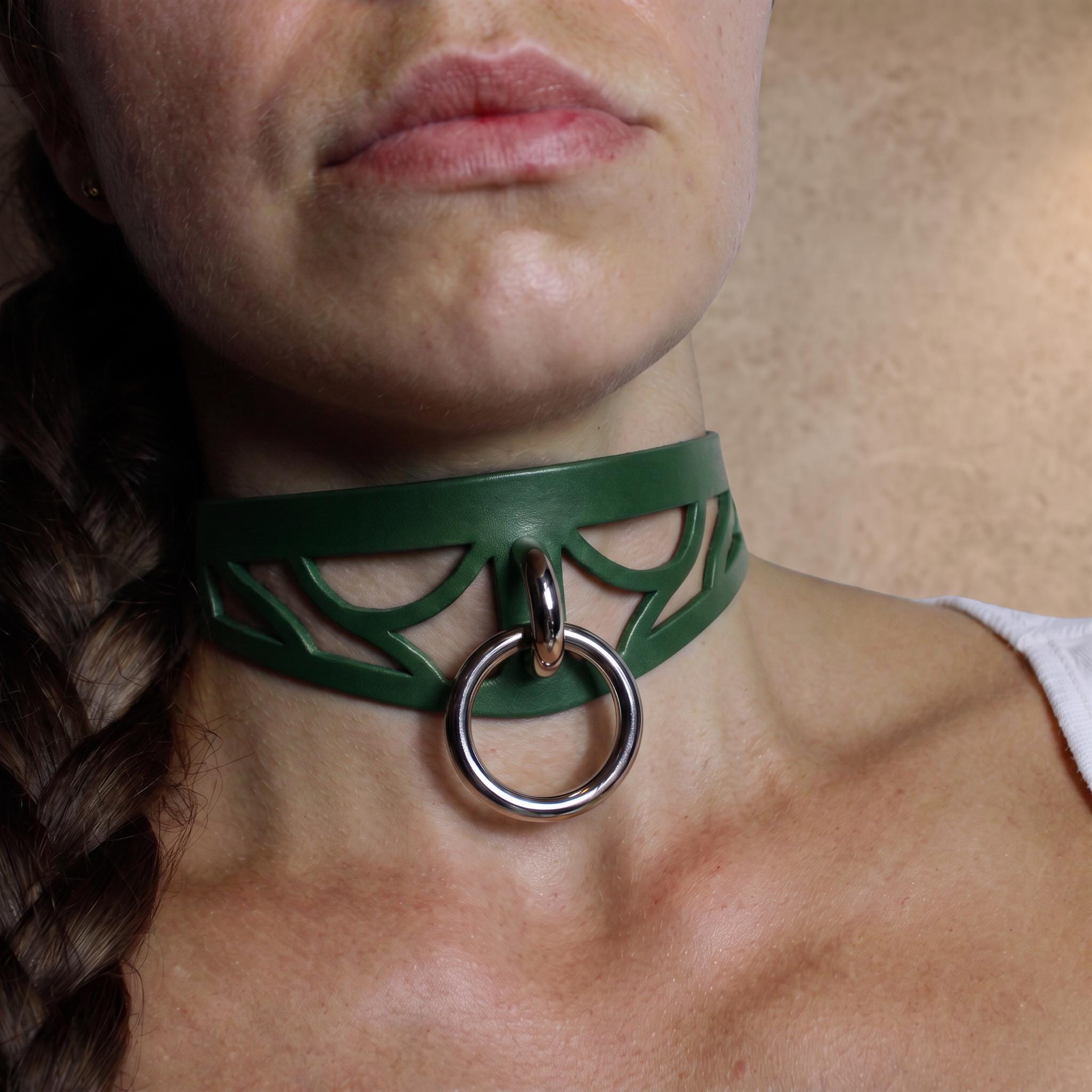 A close-up of a woman's neck and chest area, featuring a green choker necklace with a metal ring and a leaf-shaped cutout.