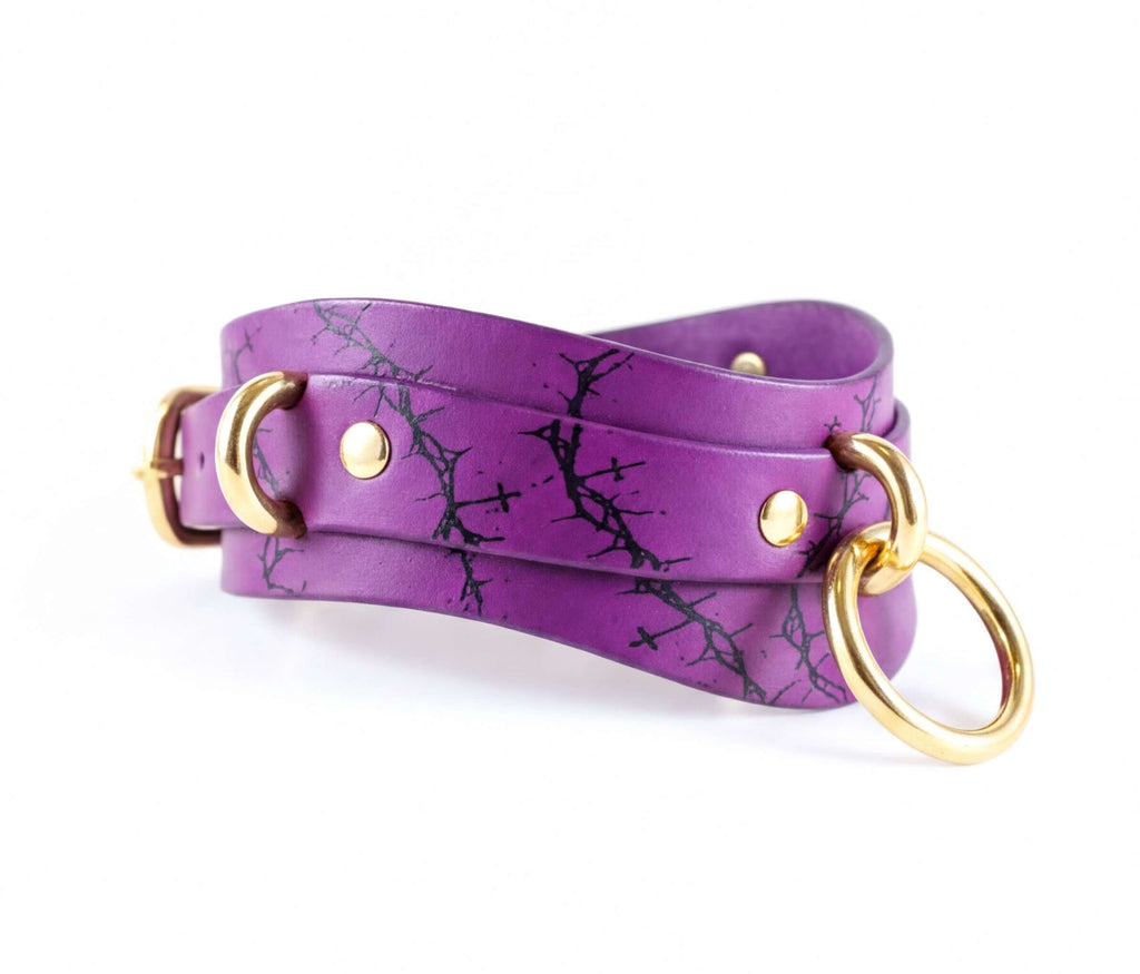 A purple leather choker necklace with a black tree branch pattern and gold-colored metal rings.
