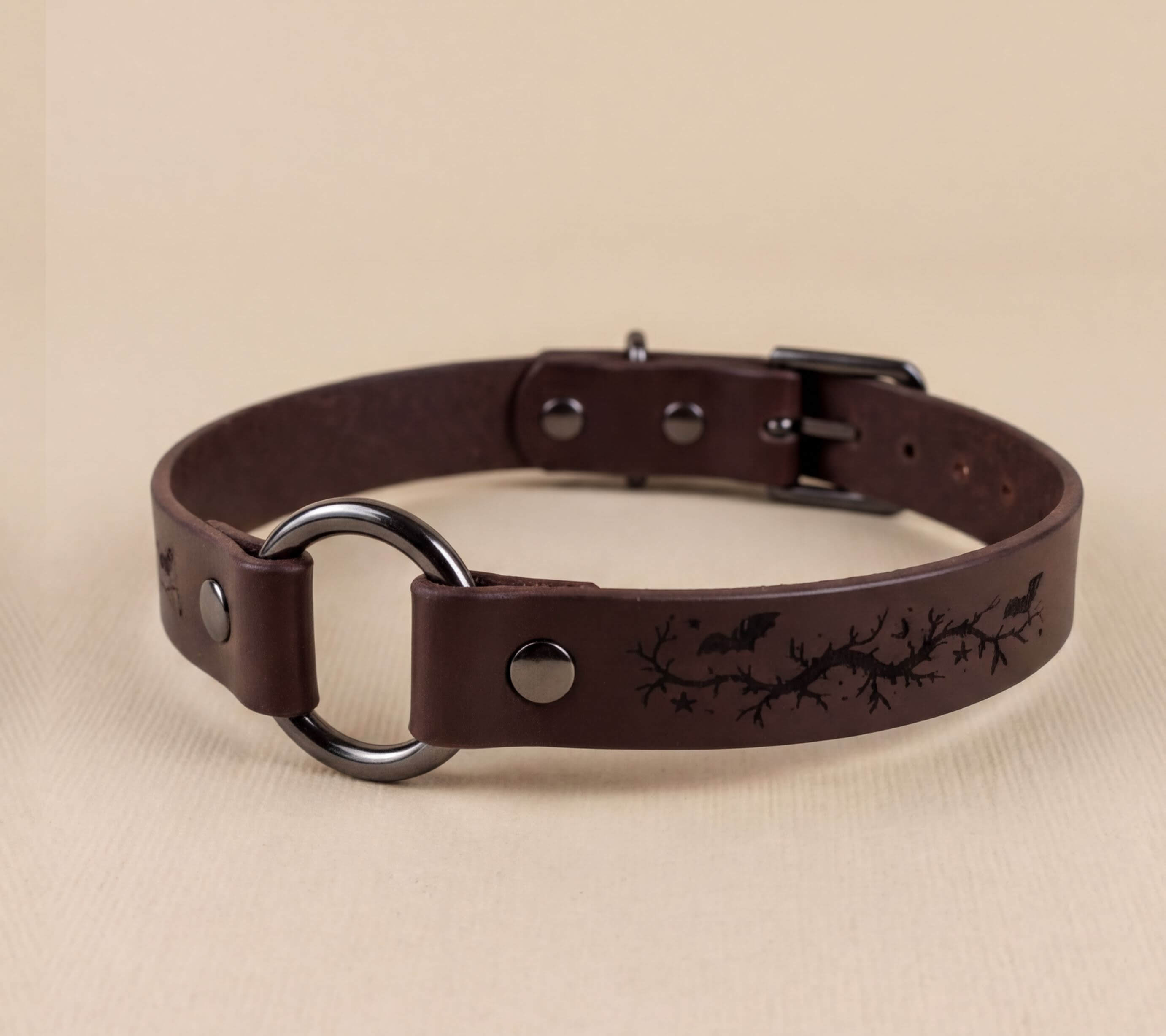 A brown leather collar with a metal ring and a design featuring bats and branches.