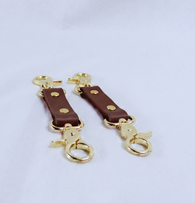 a pair of brown leather straps with gold-colored metal clasps, placed on a white surface.