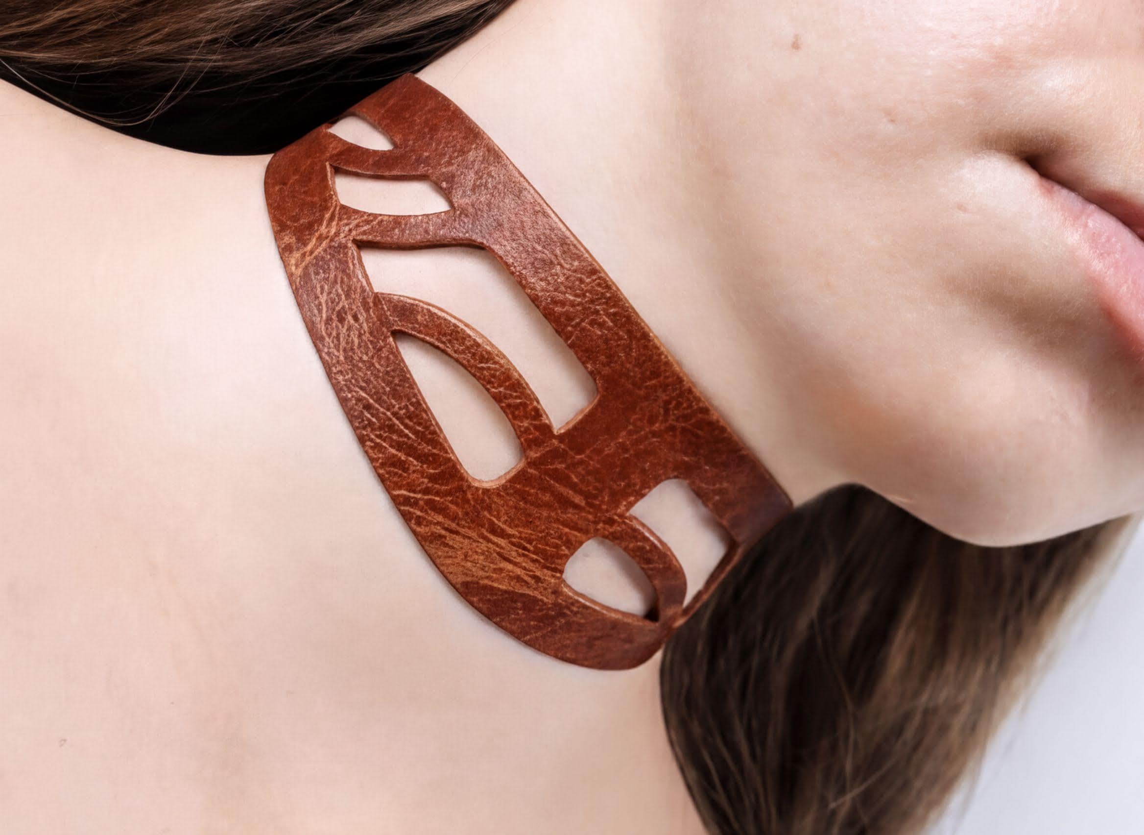 A close-up of a woman's neck wearing a brown leather choker necklace.