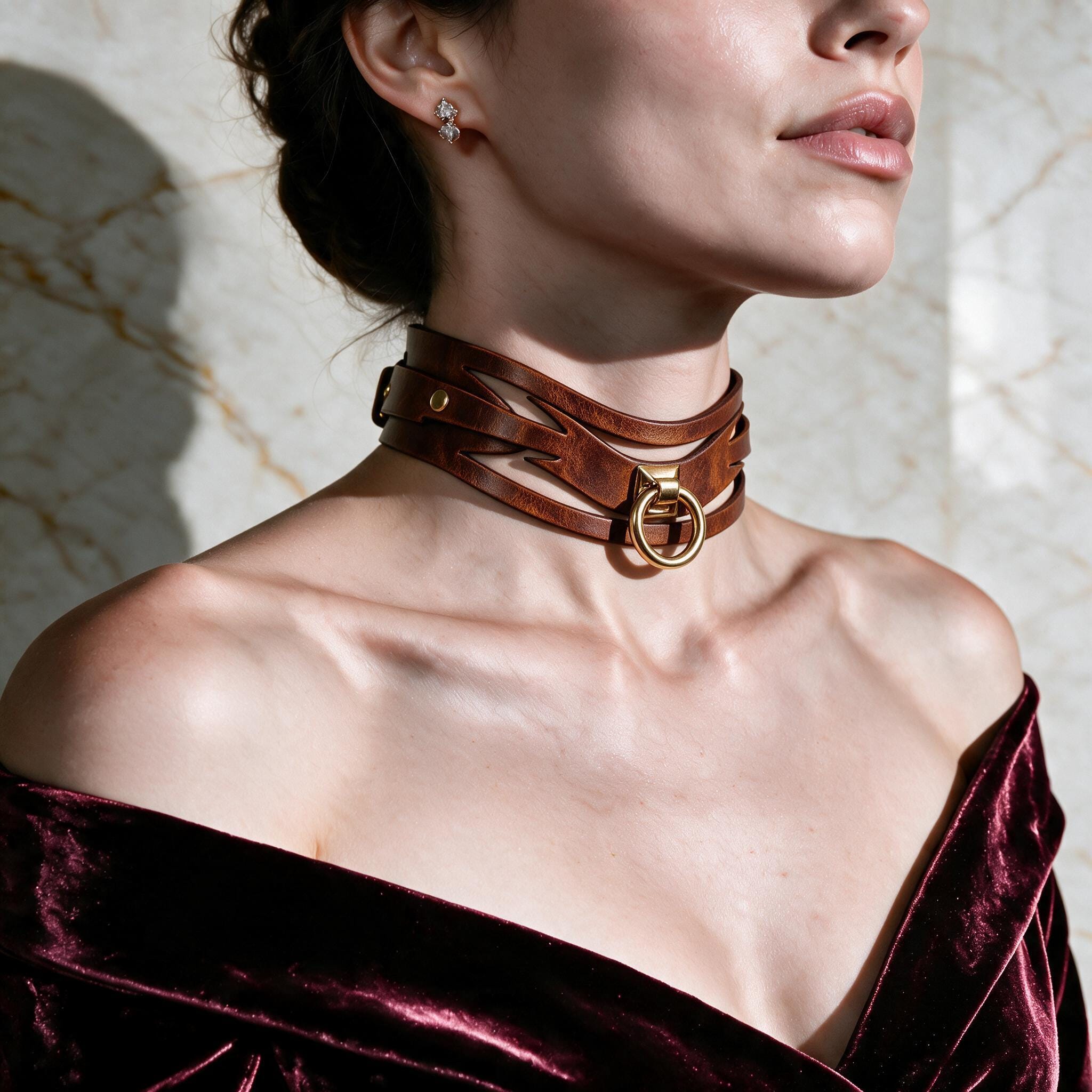A woman wearing a brown leather choker necklace with a gold buckle, posing against a marble wall.