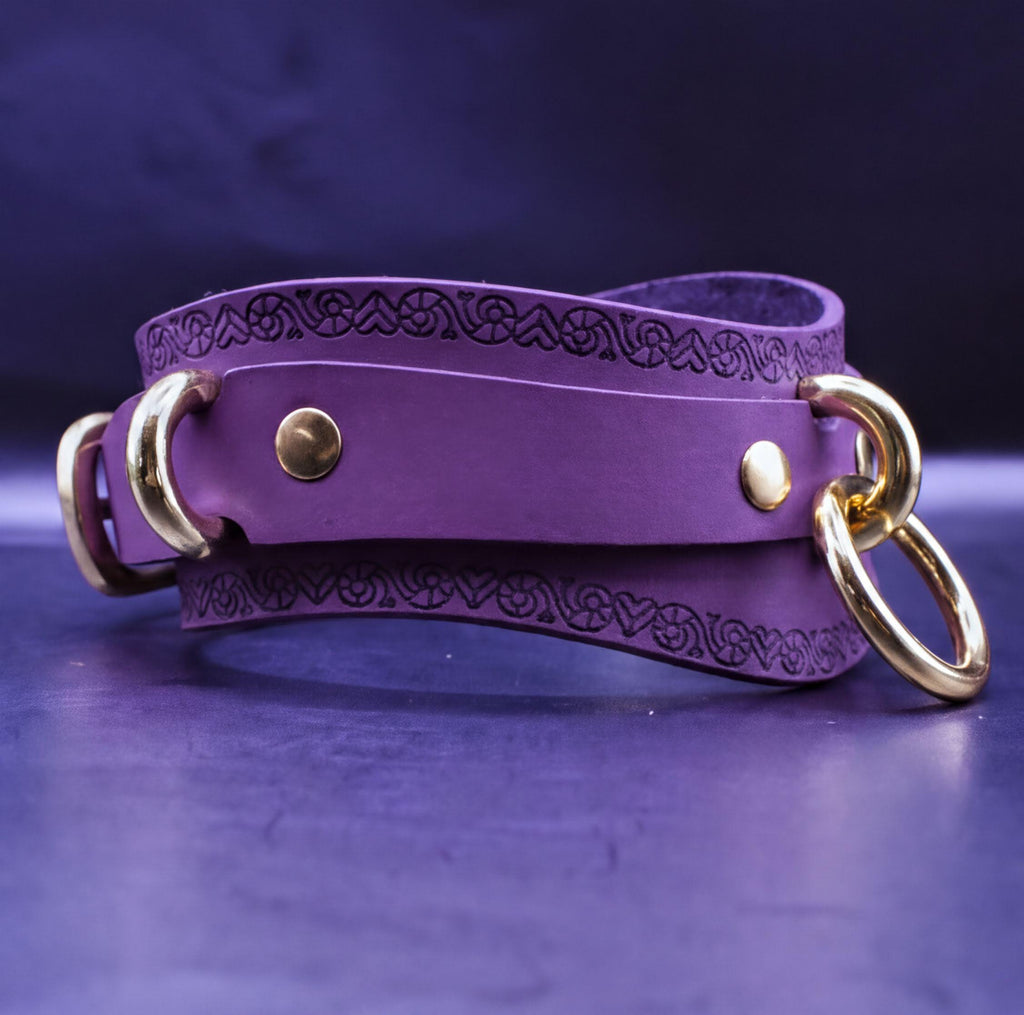 A purple leather choker necklace with gold-colored metal rings and a decorative pattern on the front.