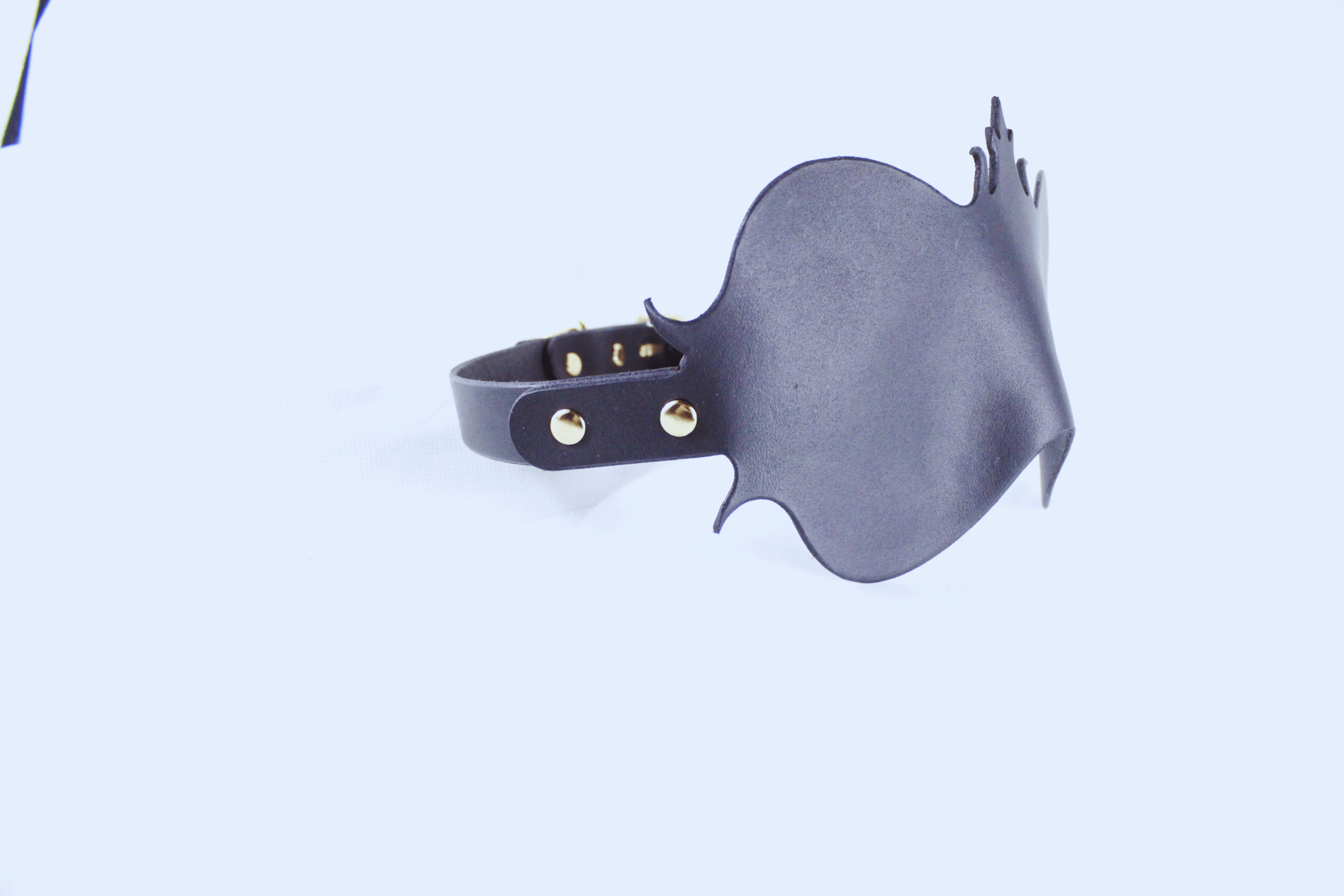 A black leather mask with a unique design, featuring a pointed top and a curved shape, is shown against a plain white background.