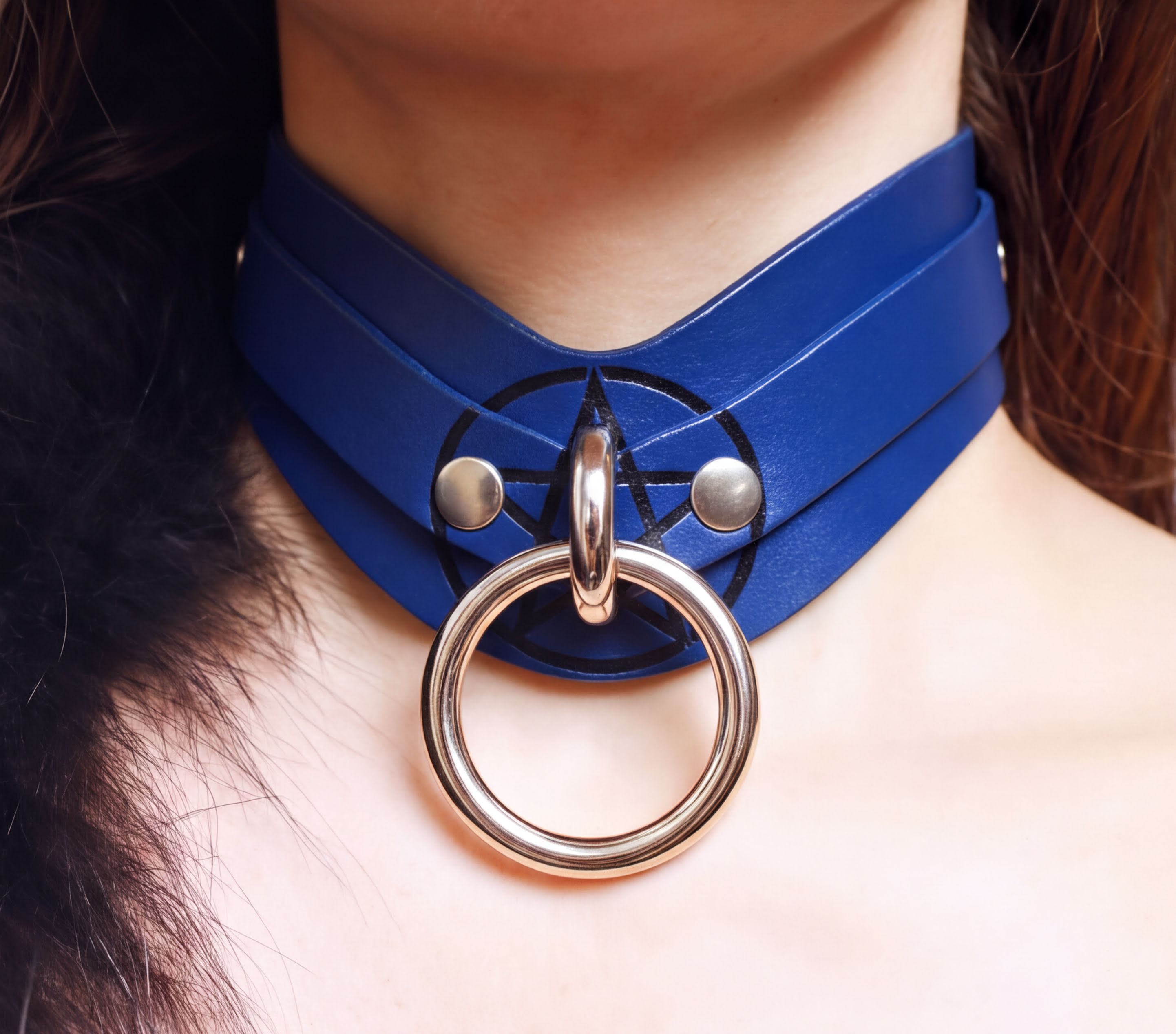 A close-up view of a person's neck and chest area wearing a blue leather choker necklace with a large metal ring.
