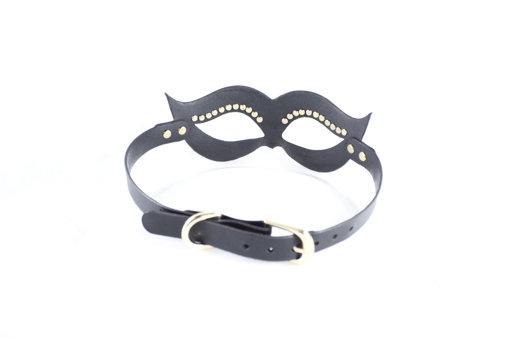 A black leather mask with gold studs on the eyes and a black strap with a gold buckle.
