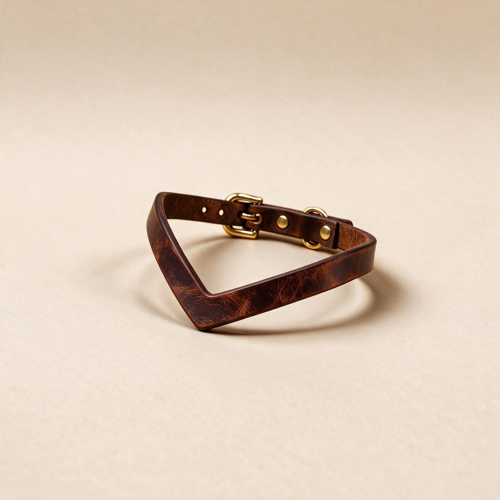 A brown leather bracelet with a gold buckle is shown against a light beige background.