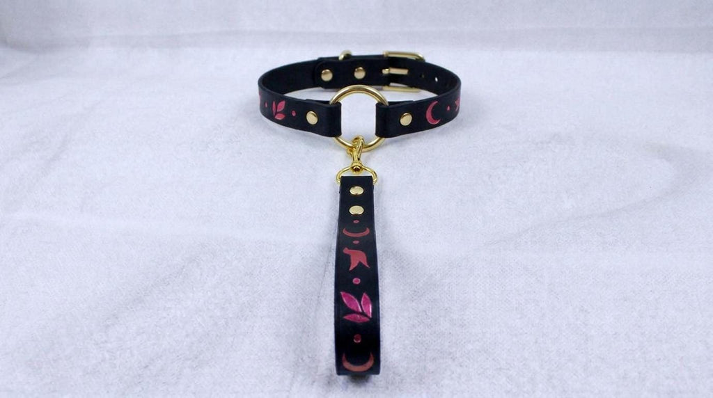 A black collar with a gold-colored buckle and a pink and black floral pattern on the strap.