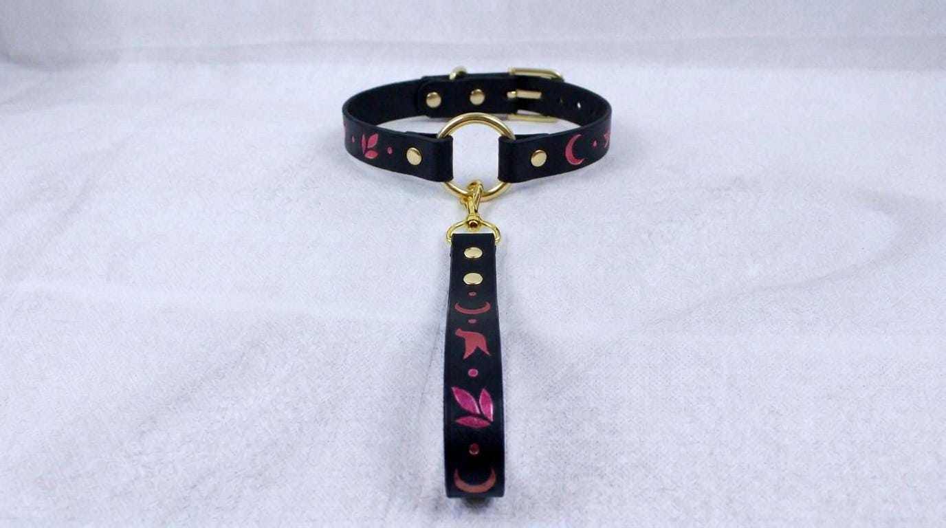 A black collar with a gold-colored buckle and a pink and black floral pattern on the strap.