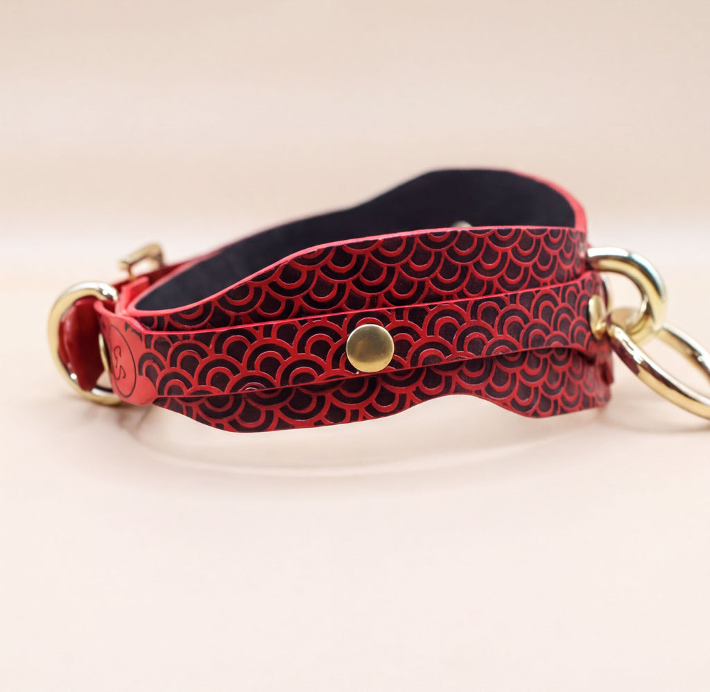 A red and black patterned leather collar with a gold buckle.