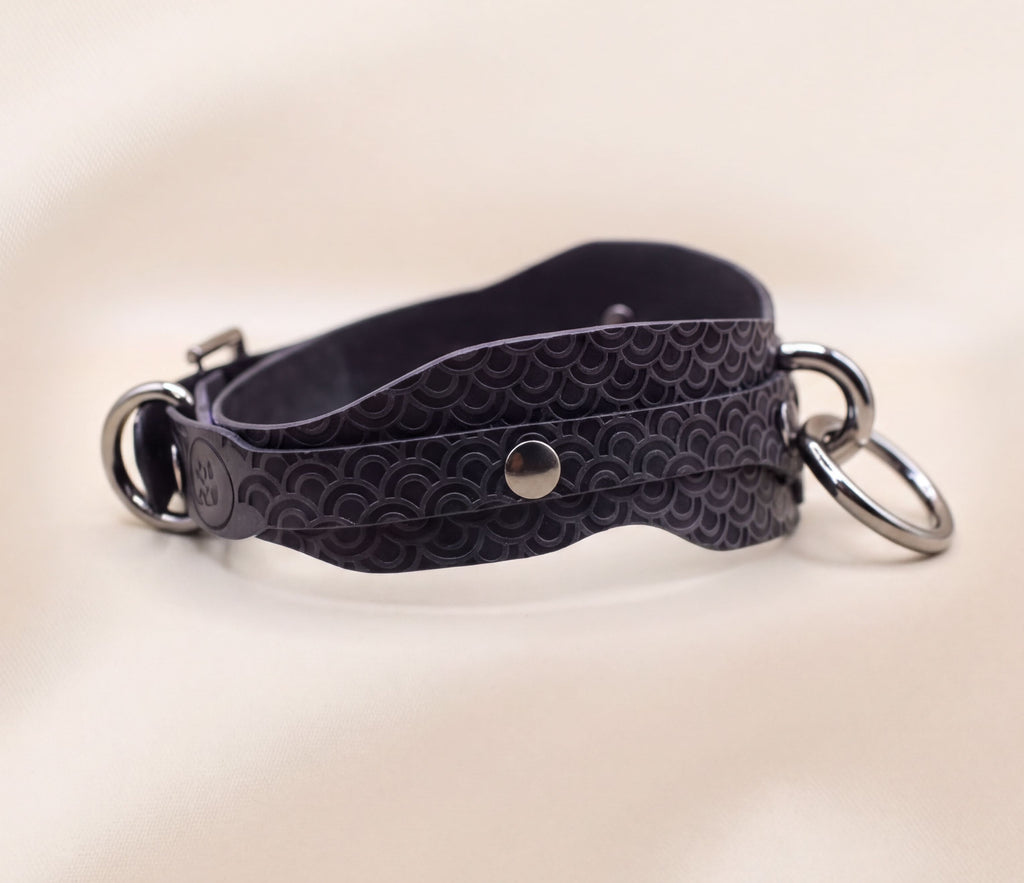 A black leather strap with metal rings and a metal buckle is shown in the image.