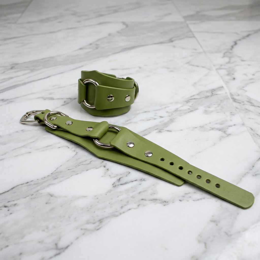 a pair of green leather straps with metal buckles, laid out on a marble surface.