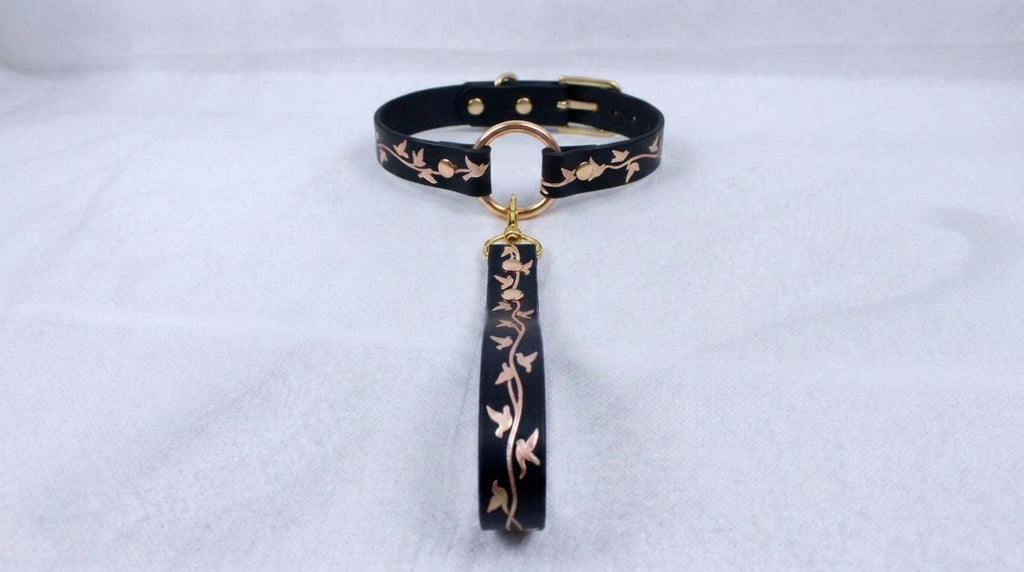 A black collar with a gold-colored metal clasp and a decorative floral pattern on the strap.