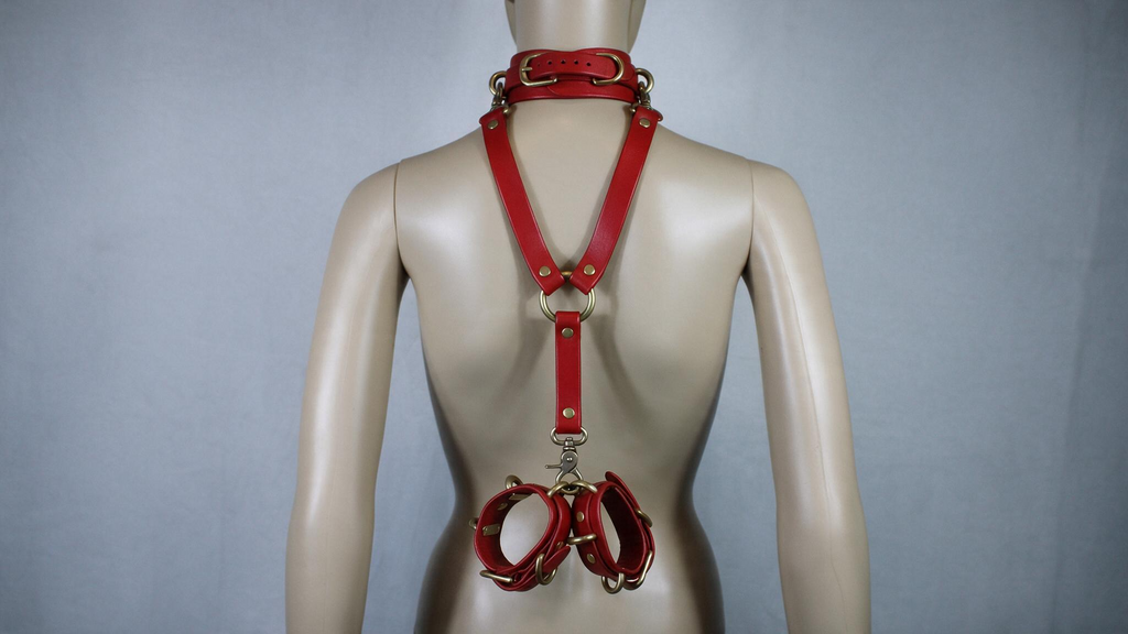A mannequin wearing a red leather harness with multiple straps and buckles, including a collar and a cinched waist.
