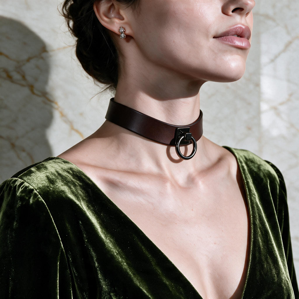 A woman wearing a green velvet dress with a choker necklace and earrings, posing against a marble wall.
