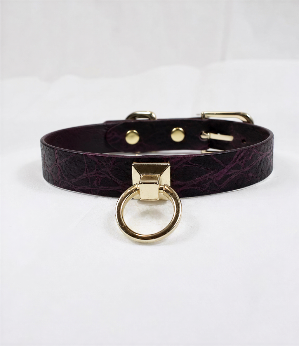 A dark purple leather choker collar with a gold-colored metal ring and buckle.