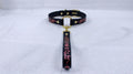 A black leather collar with a gold-colored buckle and a decorative handle attached to it, resting on a white surface.