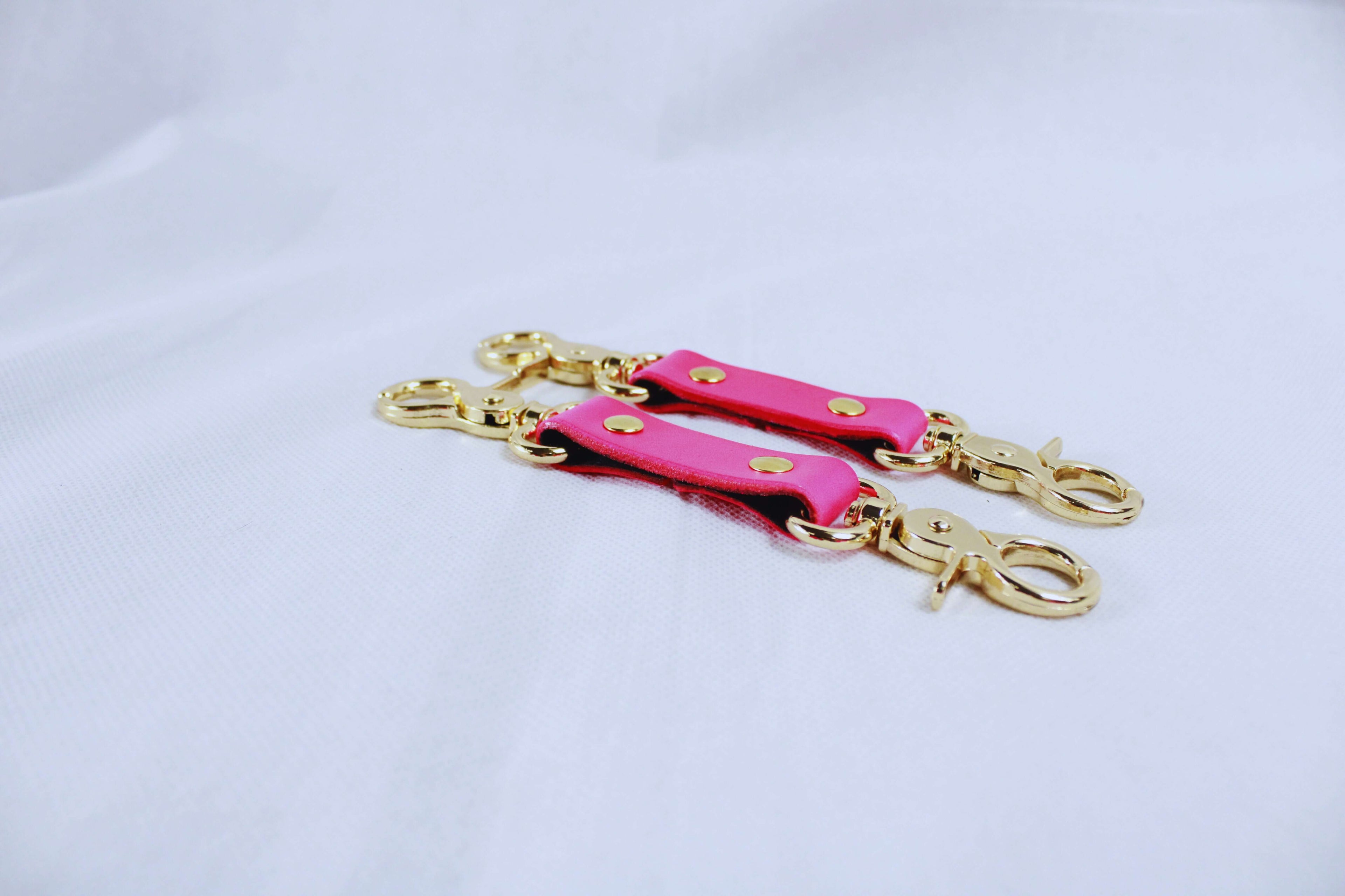 Pink bondage gear connectors with gold clasps for secure attachments in BDSM play.