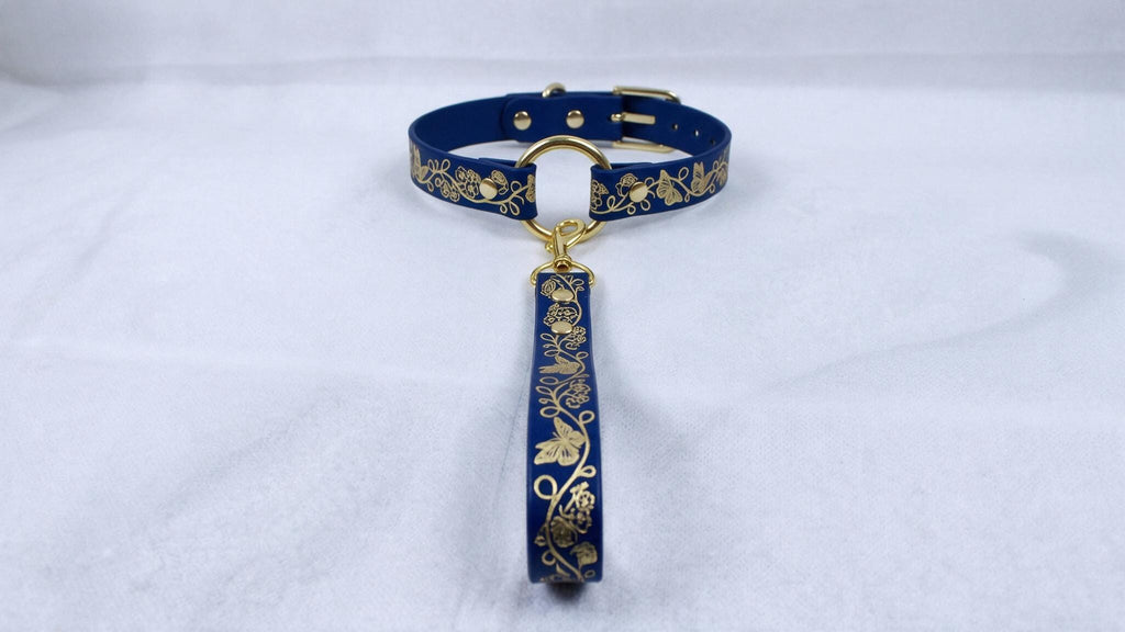 A blue collar with gold floral designs and a gold-colored tag attached to it.