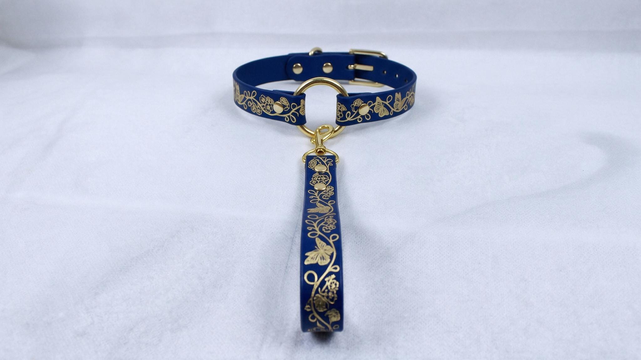 A blue collar with gold floral designs and a gold-colored tag attached to it.