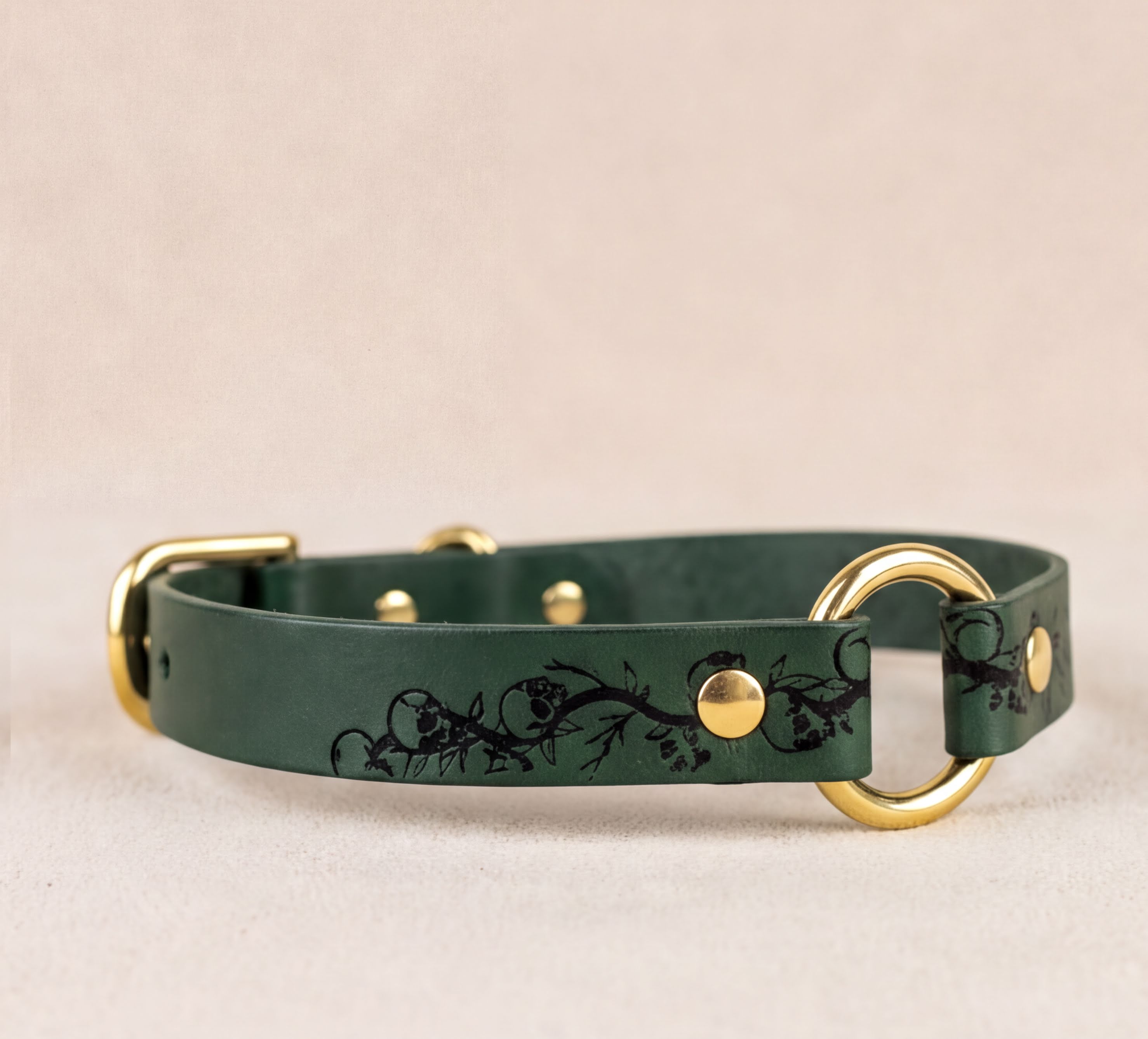 A green leather dog collar with a gold-colored buckle and a black floral design on the front.